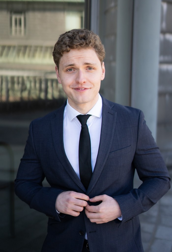 Lukas Baeskow lächelt im Anzug wie eine energiegeladene, vertrauenswürdige Person