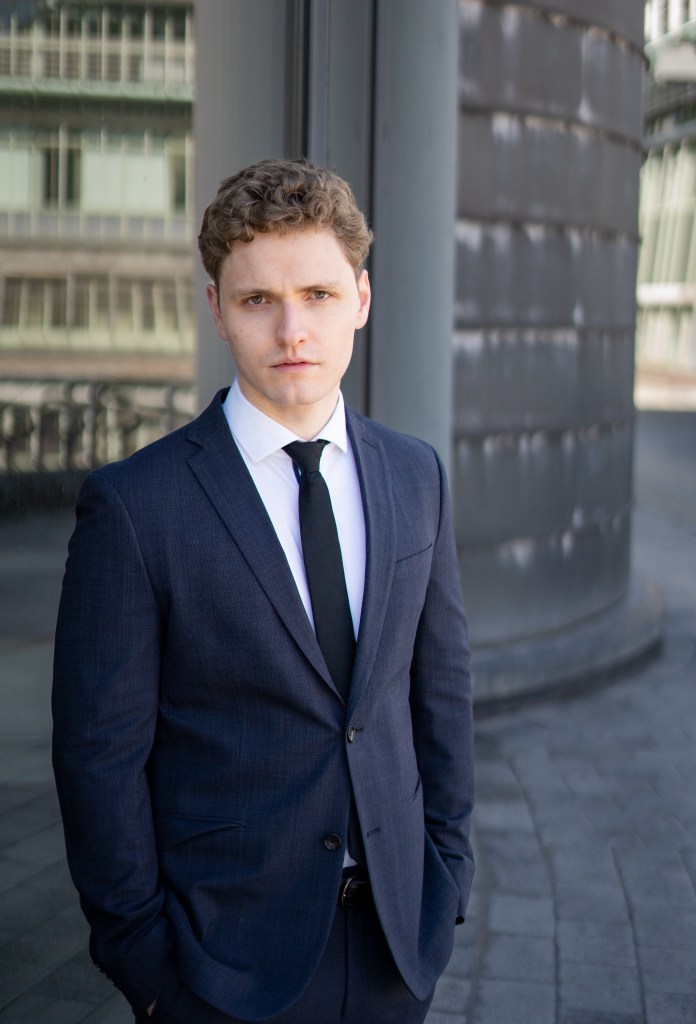 Lukas Baeskow schaut düster im Anzug mit Krawatte wie ein Bösewicht