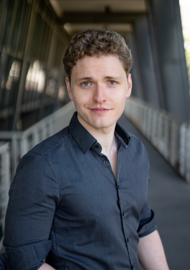 Lukas Baeskow schaut selbstbewusst in schickem grauen Hemd