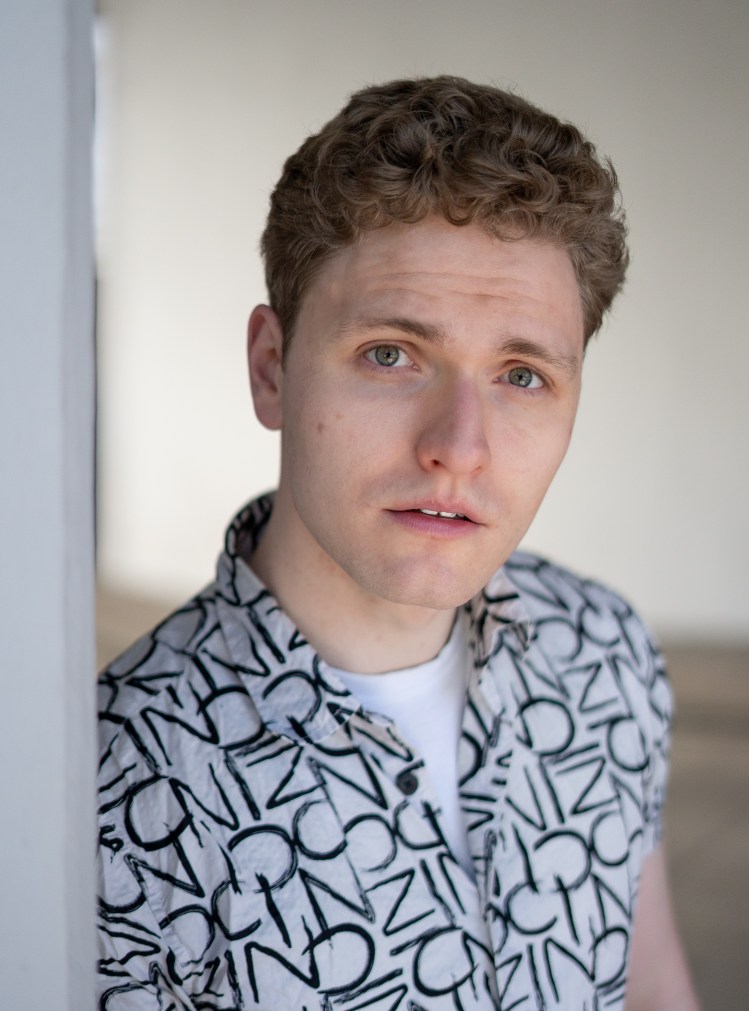 Lukas Baeskow hat einen ernsten Blick in einem weißen Hemd mit Muster